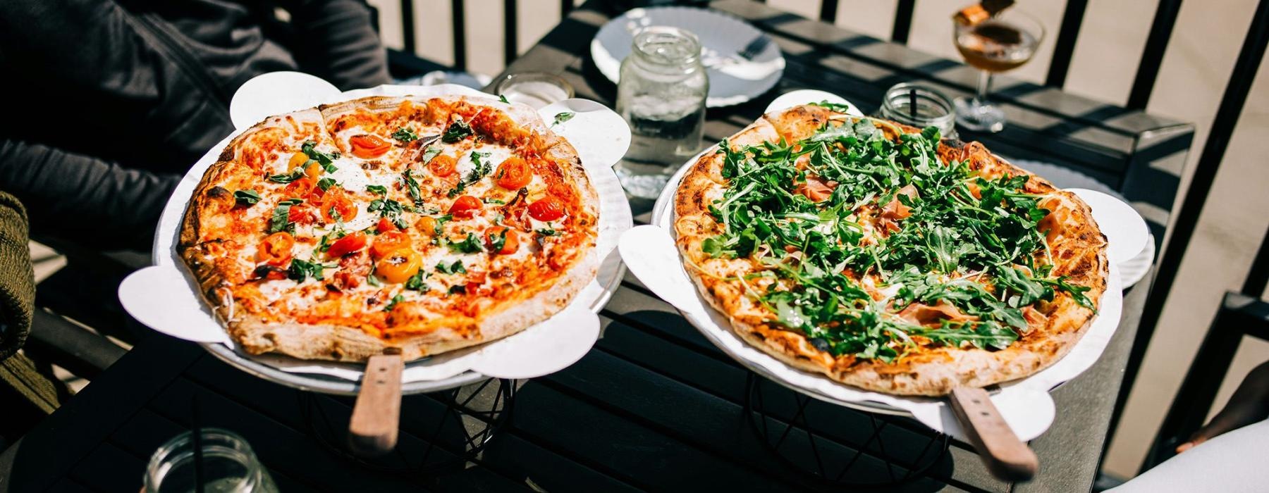 Two people with pizzas at a table outside